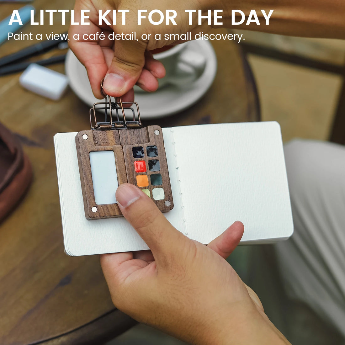 Small wooden EXPLORER palette clipped to an open journal during a painting session