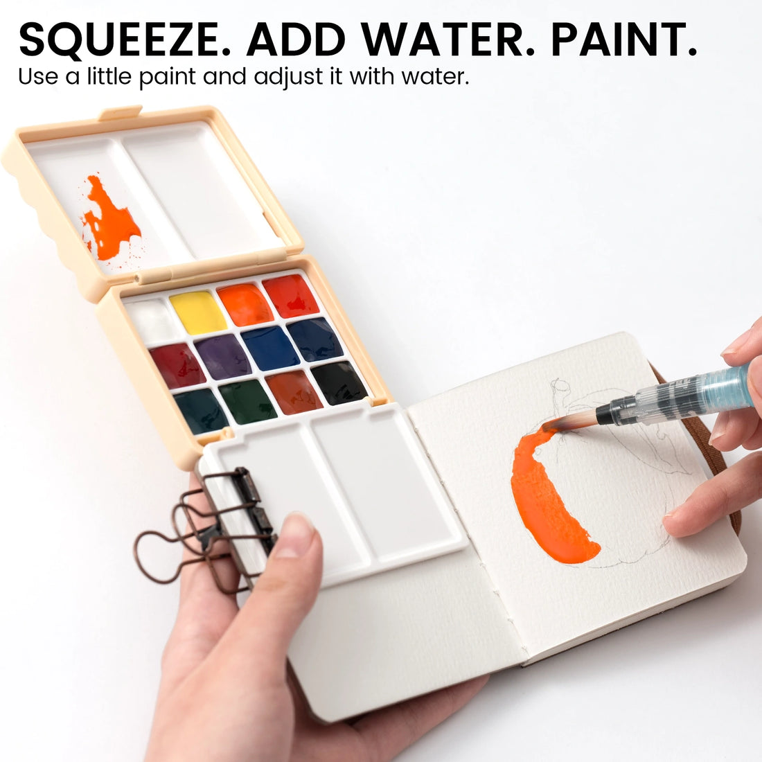 Painting an orange shape in a small journal beside a portable watercolor palette