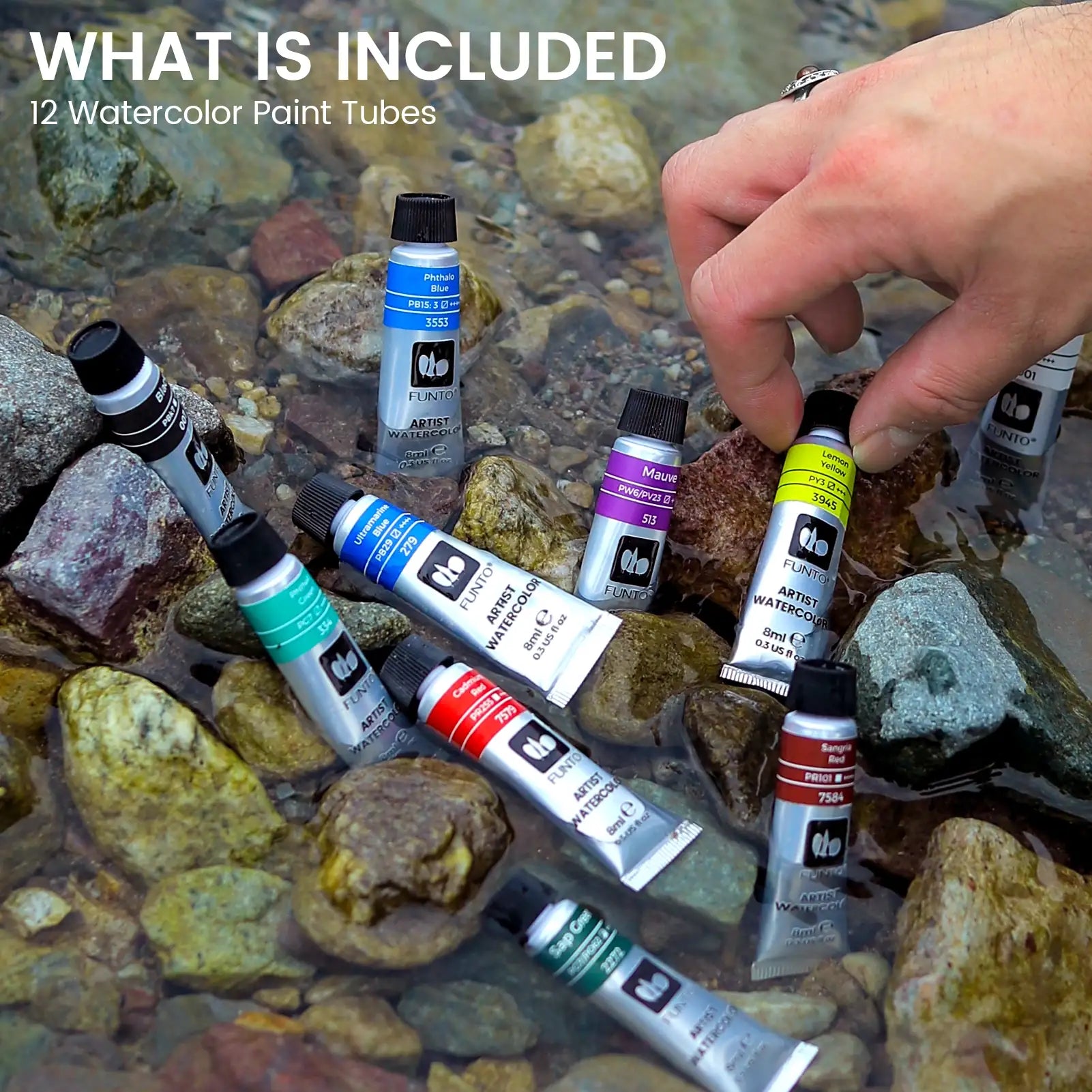 Hand selecting a watercolor tube from a set arranged on stream rocks