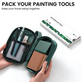 Open green EXPLORER pouch showing painting tools and journal beside a box of watercolor tubes