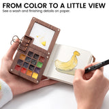Painting a yellow duck in a small journal beside a wooden watercolor palette